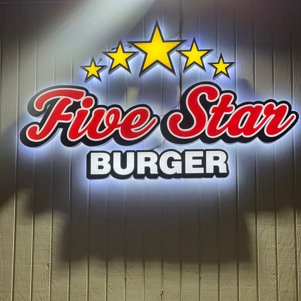Illuminated Five Star Burger sign with red lettering and yellow stars on a light-colored wooden wall.