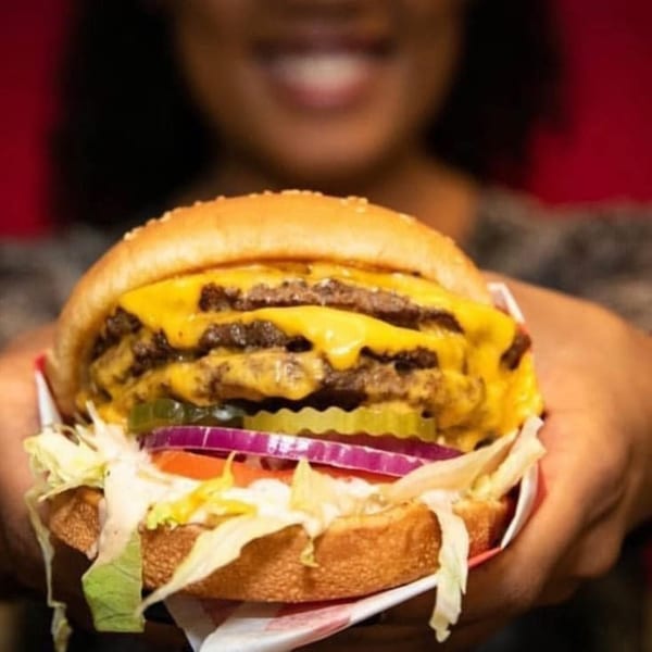 A person holds a Five Star Burger with two patties, melted cheese, lettuce, tomato, onion, and pickles.