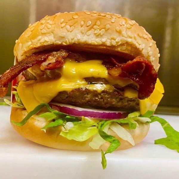 A Five Star Burger with two patties, melted cheese, bacon, red onion, and lettuce on a sesame bun.