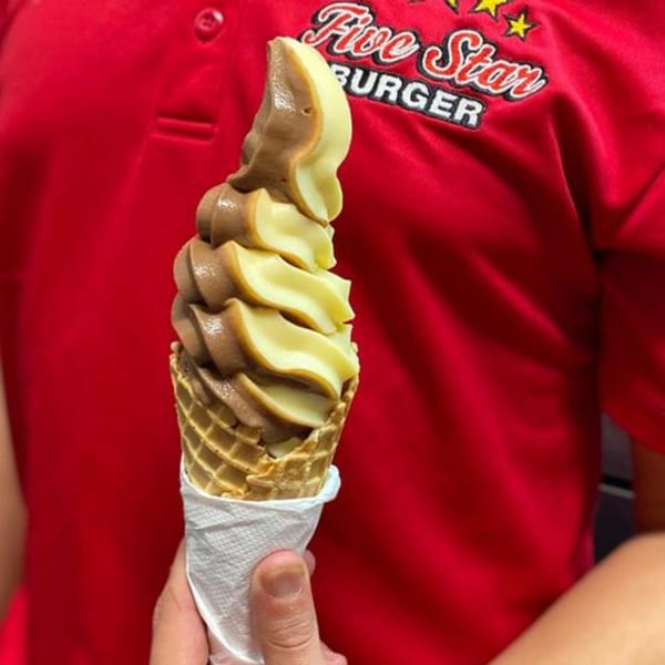Hand holding a swirl of chocolate and vanilla soft-serve ice cream in a waffle cone.