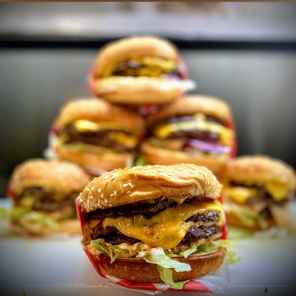 A close-up of a Five Star Burger with two patties, cheese, lettuce, and sauce, with more burgers blurred in the background.