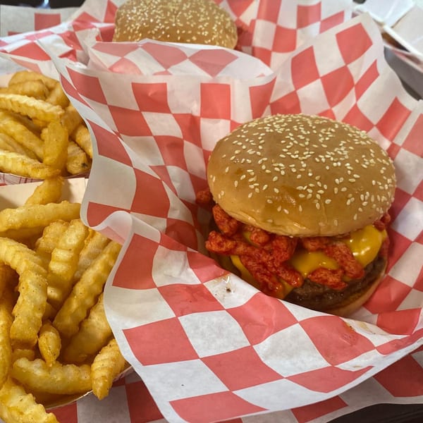 Two Five Star Burgers with cheese and red crispy toppings, and crinkle-cut fries in checkered paper.
